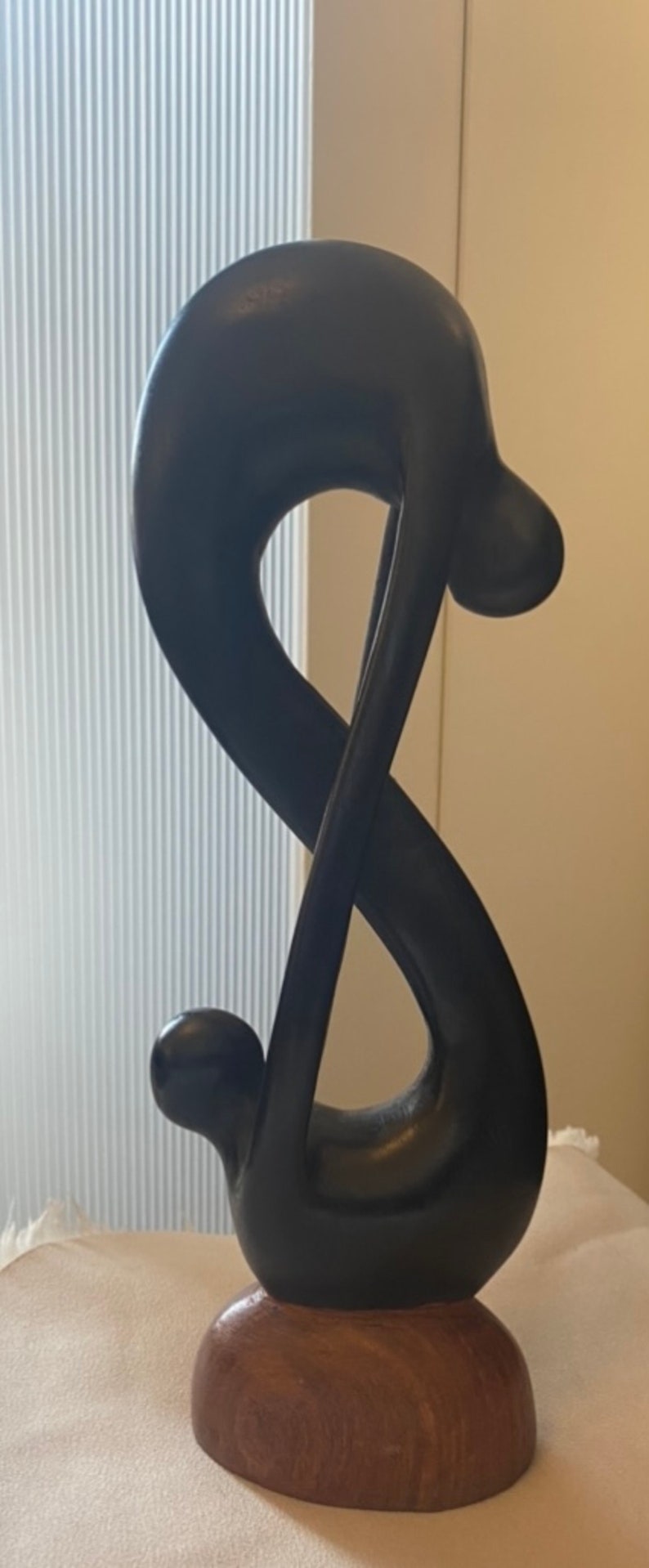 Pode incluir: Uma escultura de madeira preta de uma figura abstrata com uma base arredondada. A escultura tem a forma de um s&iacute;mbolo de infinito.