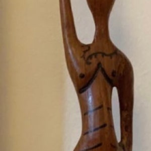 Pode incluir: Uma escultura de madeira de uma mulher carregando uma cesta na cabe&ccedil;a. A escultura &eacute; pintada em tons de marrom, vermelho e preto.