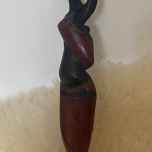 Pode incluir: Uma escultura de madeira de duas figuras, uma em p&eacute; sobre a outra. As figuras s&atilde;o estilizadas e abstratas, a figura superior tem uma cabe&ccedil;a grande e a figura inferior tem uma saia longa e fluida. A escultura &eacute; pintada em tons de marrom e preto.