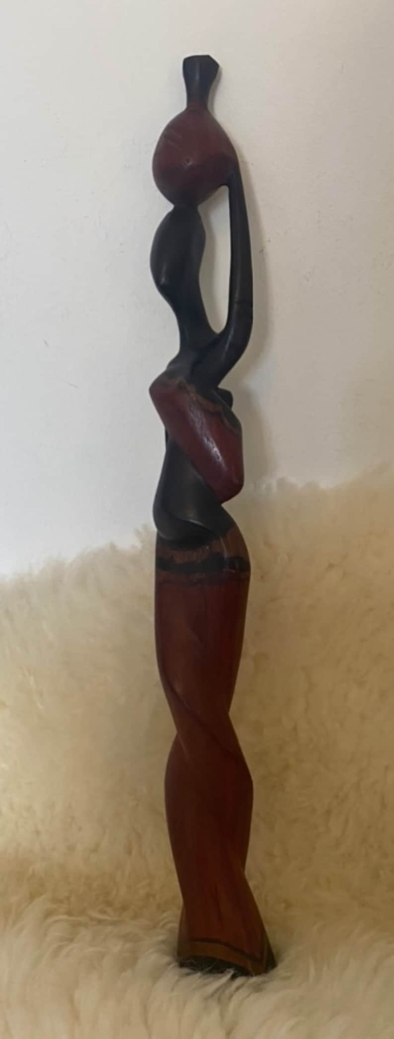 Pode incluir: Uma escultura de madeira de duas figuras, uma em p&eacute; sobre a outra. As figuras s&atilde;o estilizadas e abstratas, a figura superior tem uma cabe&ccedil;a grande e a figura inferior tem uma saia longa e fluida. A escultura &eacute; pintada em tons de marrom e preto.
