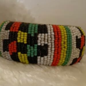 Puede incluir: Un brazalete de cuentas de colores con un patrón geométrico en negro, blanco, rojo, amarillo y verde.
