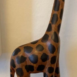 Pode incluir: Uma figura de girafa de madeira com um padr&atilde;o de manchas marrons e pretas. A girafa est&aacute; em p&eacute; sobre uma superf&iacute;cie preta.