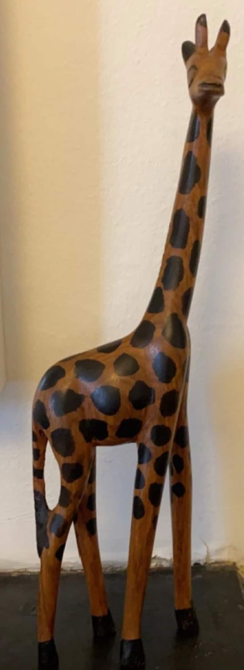 Pode incluir: Uma figura de girafa de madeira com um padr&atilde;o de manchas marrons e pretas. A girafa est&aacute; em p&eacute; sobre uma superf&iacute;cie preta.