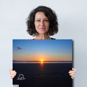 Waves form a curtain from horizon to horizon as the sunset creates a spectacular, colorful display of oranges, and yellows as it sets over Playa Tamarindo, Costa Rica. A woman holds a 16x20 inch print for perspective.