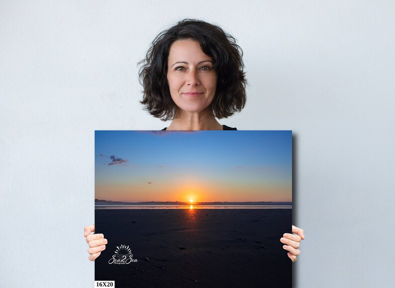 Waves form a curtain from horizon to horizon as the sunset creates a spectacular, colorful display of oranges, and yellows as it sets over Playa Tamarindo, Costa Rica. A woman holds a 16x20 inch print for perspective.