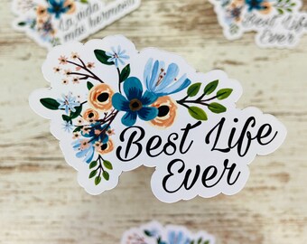 May include: A white sticker with a floral design and the text "Best Life Ever". The flowers are blue, orange, and green.