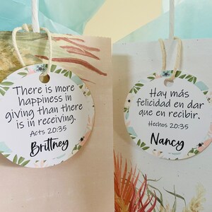 K&ouml;nnte beinhalten: Zwei runde Geschenkanh&auml;nger mit Blumendesigns. Der Anh&auml;nger links sagt "There is more happiness in giving than there is in receiving. Acts 20:35" und ist mit "Brittney" signiert. Der Anh&auml;nger rechts sagt "Hay m&aacute;s felicidad en dar que en recibir. Hechos 20:35" und ist mit "Nancy" signiert.