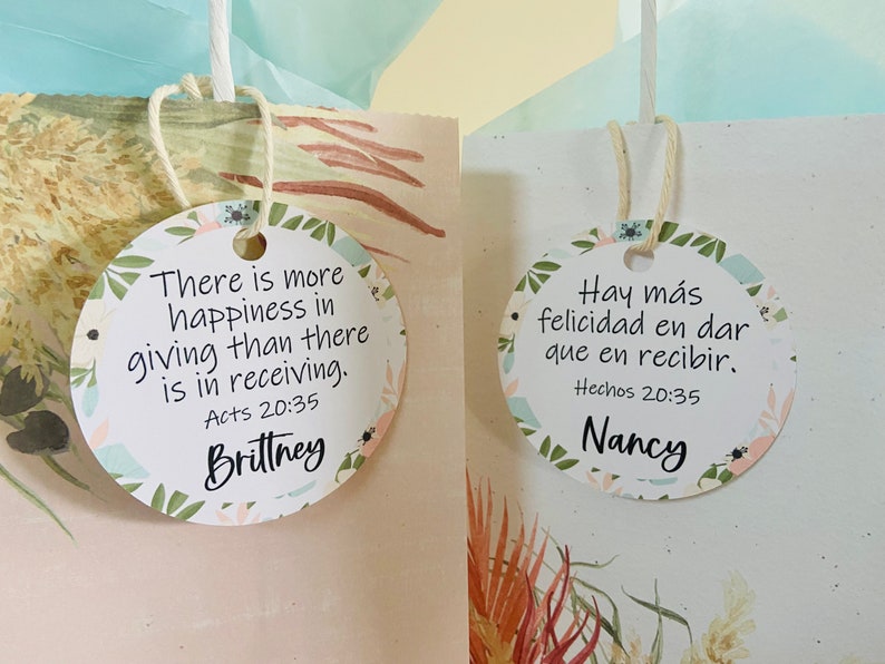 K&ouml;nnte beinhalten: Zwei runde Geschenkanh&auml;nger mit Blumendesigns. Der Anh&auml;nger links sagt "There is more happiness in giving than there is in receiving. Acts 20:35" und ist mit "Brittney" signiert. Der Anh&auml;nger rechts sagt "Hay m&aacute;s felicidad en dar que en recibir. Hechos 20:35" und ist mit "Nancy" signiert.