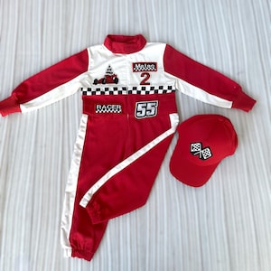 Puede incluir: Un mono de carreras rojo y blanco con gorra de béisbol roja a juego. El mono presenta un diseño de bandera a cuadros, el número 2 y el nombre "Mateo". La gorra tiene un emblema de bandera a cuadros. El conjunto está diseñado para niños.