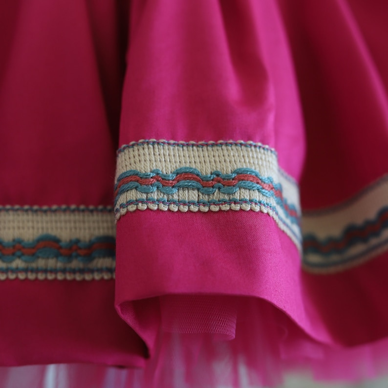 K&ouml;nnte beinhalten: Nahaufnahme eines rosa Rocks mit einem wei&szlig;en und blauen Besatz. Der Besatz hat ein wellenf&ouml;rmiges Design und ist auf den Rock gen&auml;ht.