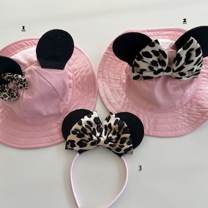 May include: Two pink sun hats with black ears and leopard print bows. A headband with black ears and a leopard print bow.