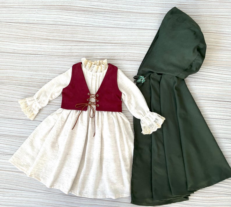 May include: A cream-colored dress with a burgundy vest and a dark green hooded cape. The dress has long sleeves with lace trim and a lace-trimmed collar. The vest has a laced front. The cape is fastened with a decorative clasp.