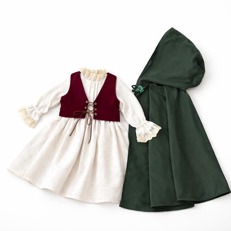 May include: A cream-colored dress with long sleeves and lace trim, paired with a burgundy vest and a dark green hooded cloak. The vest has a lace-up front. The cloak has a decorative leaf clasp.