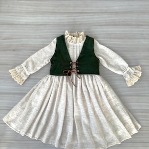 May include: A light-colored dress with long sleeves and a flared skirt. The dress features a dark green vest with a lace-up front and a high, ruffled collar. The sleeves and collar are trimmed with lace.