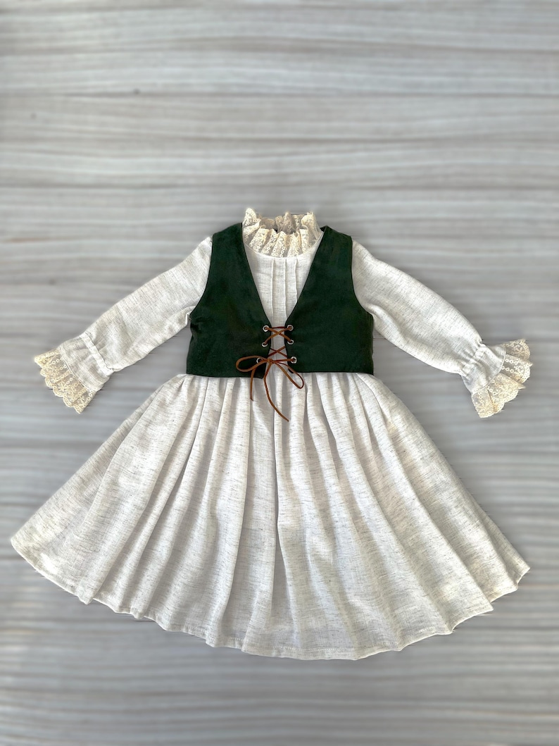 May include: A light-colored dress with long sleeves and a flared skirt. The dress features a dark green vest with a lace-up front and a high, ruffled collar. The sleeves and collar are trimmed with lace.
