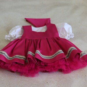 K&ouml;nnte beinhalten: Ein rosa Kleid mit einem wei&szlig;en Oberteil und einem Volantrock. Das Kleid hat einen wei&szlig;en Kragen und ein rosa Band um die Taille. Das Kleid ist aus einem weichen, flie&szlig;enden Stoff.