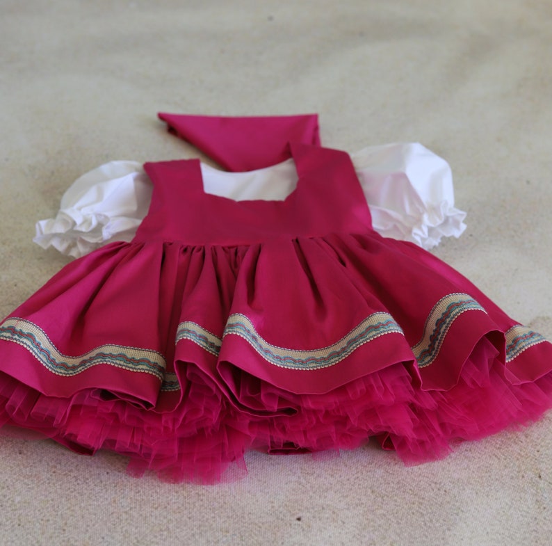K&ouml;nnte beinhalten: Ein rosa Kleid mit einem wei&szlig;en Oberteil und einem Volantrock. Das Kleid hat einen wei&szlig;en Kragen und ein rosa Band um die Taille. Das Kleid ist aus einem weichen, flie&szlig;enden Stoff.