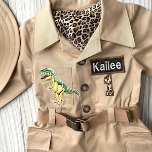 Pu&ograve; includere: Una tuta da safari beige con una toppa di dinosauro, una fodera con stampa leopardata e un'etichetta con il nome "Kailee".
