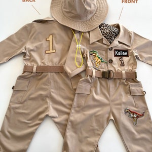 Pu&ograve; includere: Una tuta da safari beige con una toppa di dinosauro sulla gamba destra, un'etichetta con il nome "Kallie" e il numero "1" sul retro. La tuta ha una cintura e due tasche sul davanti. &Egrave; incluso un cappello da safari beige.