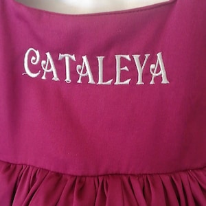 Peut inclure: Une robe bordeaux avec un nom brod&eacute; en blanc "CATALEYA" sur le corsage.