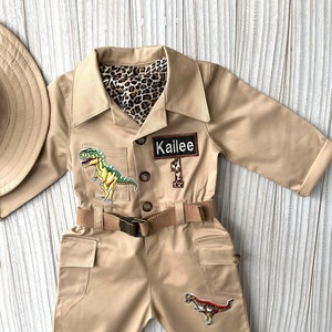 Pu&ograve; includere: Una tuta da safari beige con una cintura marrone, due toppe di dinosauro e un'etichetta con il nome "Kailee".
