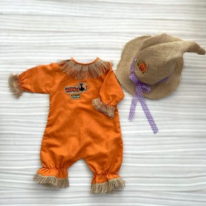 Peut inclure: Un costume d'Halloween orange pour bébé ou jeune enfant, comprenant une combinaison à manches longues avec des bordures à franges et un chapeau de paille assorti. La combinaison porte le nom "Oliver" et le mot "Halloween".