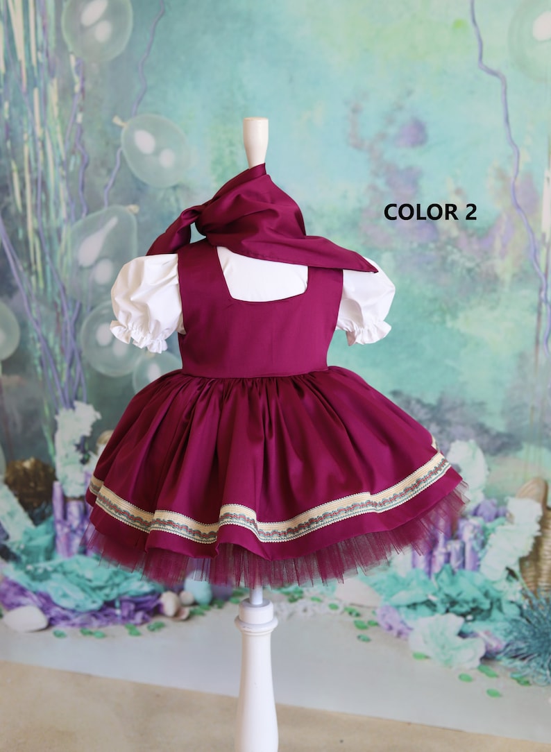Peut inclure: Une robe bordeaux avec un chemisier blanc et un foulard bordeaux. La robe est orn&eacute;e d'une bordure blanche et verte autour du bas. La robe est sur un mannequin blanc. Le texte "COLOR 2" est visible sur l'image.