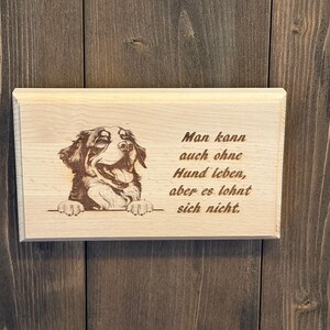 Könnte beinhalten: Rechteckige Holzplakette mit detaillierter Gravur eines Hunde-Gesichts und Pfoten. Der Text lautet: „Man kann auch ohne Hund leben, aber es lohnt sich nicht.“ Hergestellt aus hellem Holz.