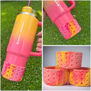 May include: A Stanley + Starbucks tumbler with a gradient design in shades of yellow, orange, and pink. The tumbler has a pink handle and a patterned pink and yellow silicone base. The image also shows three silicone bases.