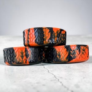 May include: Three cylindrical containers featuring a marbled black and orange color scheme. The exterior surfaces are textured with a repeating raised pattern of vertical, leaf-like shapes that wrap around the entire circumference of each item.