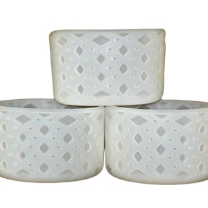 May include: Three white ceramic candle holders with a geometric diamond pattern. The holders are stacked on top of each other.