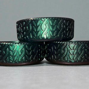 May include: Three teal-colored, decorative bowls stacked on top of each other. Each bowl has a textured, leaf-like pattern around the exterior. The bowls have a metallic sheen, and the rims are a darker shade of teal.