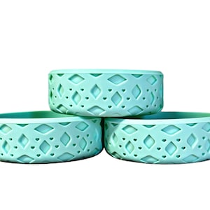 May include: Three teal blue silicone bowls with a geometric pattern. The bowls are stacked on top of each other.