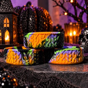 May include: Three round silicone molds featuring a raised, textured cable knit pattern. The molds are colored in a marbled blend of vibrant orange, bright purple, lime green, and black, designed for crafting or baking applications.