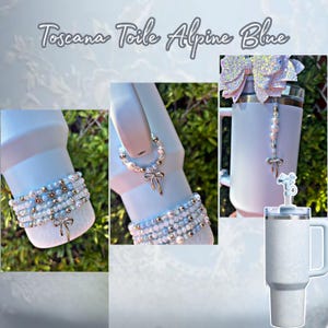 May include: A light blue tumbler with a handle, a bracelet, and a charm with a bow design. The bracelet and charm are adorned with pearls and small silver beads. The text "Toscana Toile Alpine Blue" is at the top.