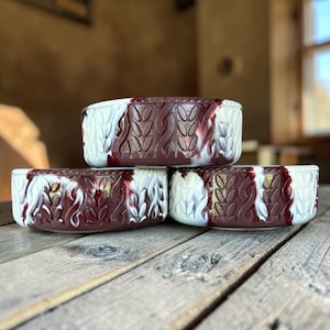 May include: Three round ceramic bowls featuring a marbled swirl pattern of deep burgundy and creamy white. The exterior surface of each bowl is embossed with a repeating vertical cable knit texture that wraps around the entire circumference.