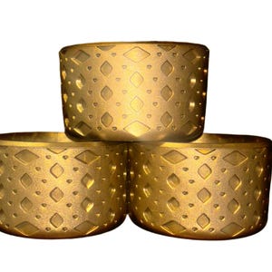 May include: Three gold-colored metal rings with a geometric pattern. The rings are stacked on top of each other.
