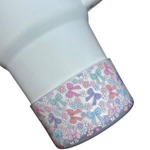 May include: White tumbler with a colorful bow and flower pattern around the bottom edge.