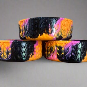 May include: Three decorative bowls with a vibrant design. The bowls are rectangular with a black base and feature a flame-like pattern in orange, pink, and purple. The bowls are stacked on top of each other.