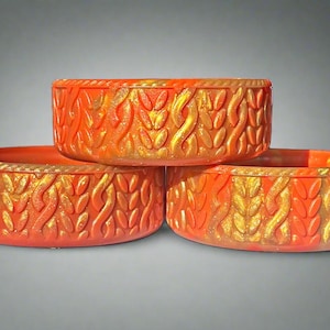 May include: Three orange decorative bowls with a textured, flame-like design and gold accents. The bowls are stacked, showcasing their intricate patterns and vibrant colors. These bowls are ideal for home decor.