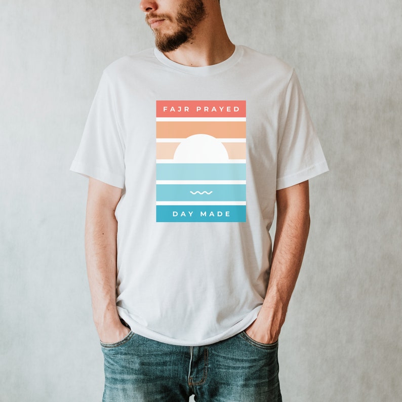 May include: White t-shirt with a graphic design featuring a sunset with the text "FAJR PRAYED DAY MADE" in a colorful, retro style.