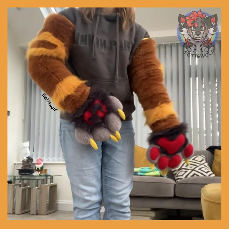 May include: A pair of long, faux fur arm sleeves featuring horizontal brown and orange stripes, paired with matching plush paw gloves. The gloves are dark gray with red paw pads and prominent yellow claws. The text Setiswolf is visible.