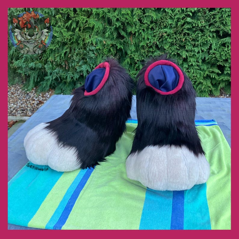 May include: Pair of black and white furry paws with blue and red accents. The paws are designed with a rounded shape and are placed on a striped green and blue towel. The image is taken outdoors.