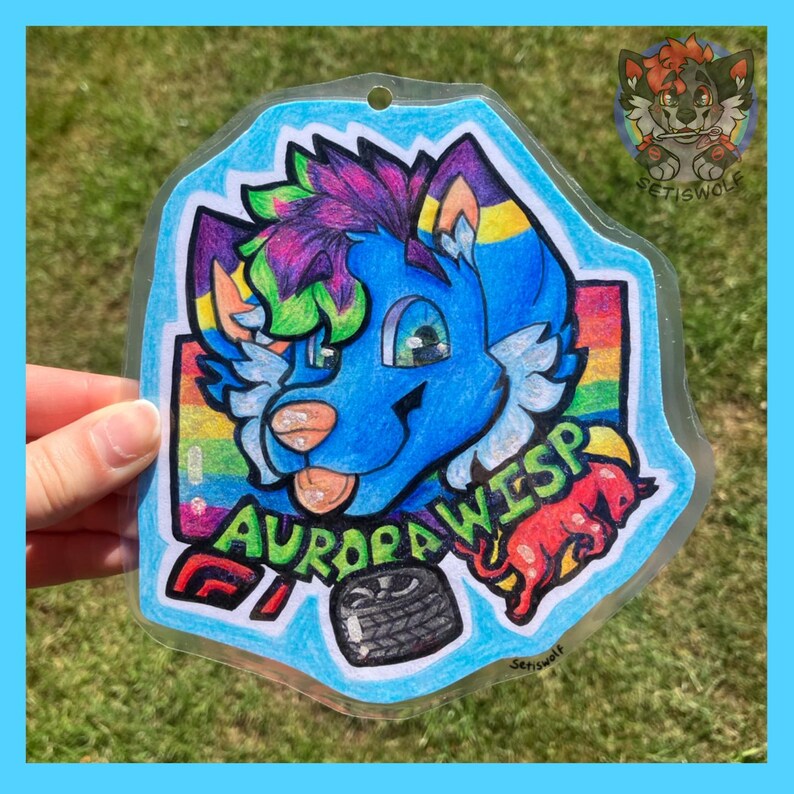 K&ouml;nnte beinhalten: Ein transparenter Acryl-Anh&auml;nger mit einer farbenfrohen Illustration eines blauen anthropomorphen Wesens mit violettem und gr&uuml;nem Haar. Das Design umfasst einen Regenbogenhintergrund, eine rote Kreaturensilhouette, einen schwarzen Reifen und den Text AURORA WISP.
