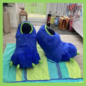 May include: A pair of blue furry monster feet slippers with green claws and trim. The slippers are resting on a green and blue striped towel. The text "Setiswolf" is visible on the towel.