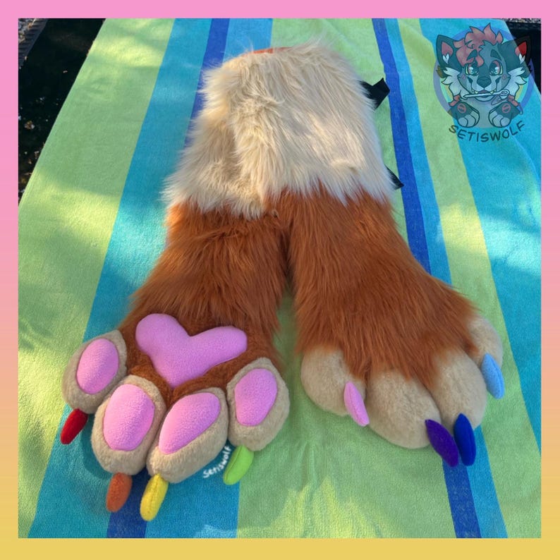 May include: A pair of faux fur hand paws featuring long orange and cream-colored fur. The paws have large pink heart-shaped palm pads, smaller pink finger pads, and multi-colored claws in red, orange, yellow, lime green, purple, and blue.