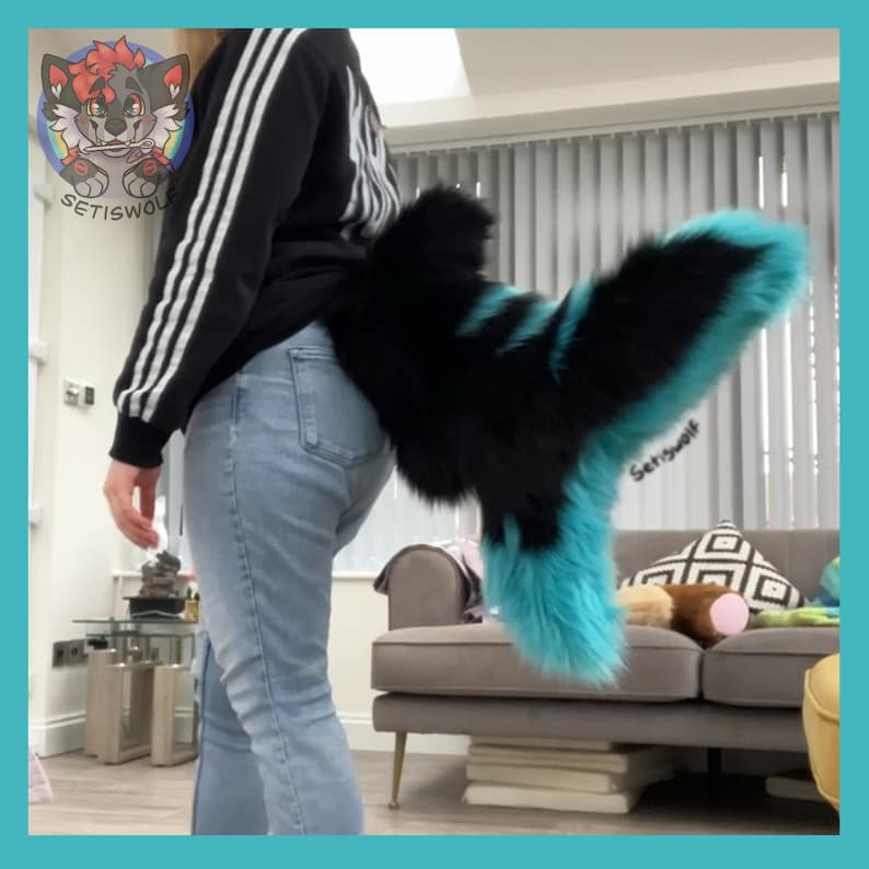 May include: A black and turquoise faux fur tail, worn by a person. The tail is attached to the back of the person's jeans. The tail has a black base with turquoise accents and a fluffy texture. The brand name "Setiswolf" is visible.
