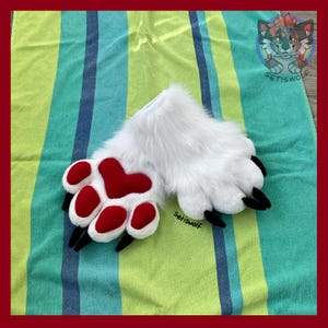 May include: A pair of white faux fur animal paw gloves featuring plush red heart-shaped and oval-shaped paw pads with black claws. The text Setiswolf is visible on the paw and in the top right corner logo, which depicts a stylized wolf character.