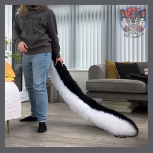 Può includere: Una lunga coda in pelliccia sintetica morbida con un design bicolore, con pelliccia nera sul lato superiore e pelliccia bianca sul lato inferiore. La coda è attaccata a una felpa grigia con cappuccio e jeans azzurri, arrivando fino al pavimento.