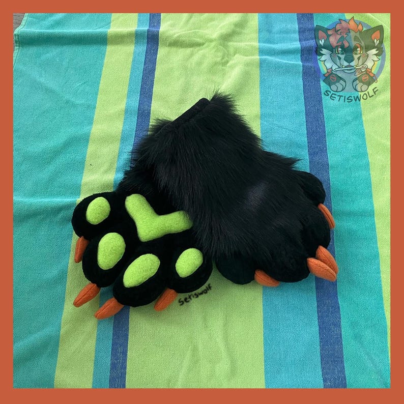 May include: A pair of black faux fur paw gloves featuring bright lime green paw pads and orange claws. The gloves are designed with long black fur on the back and include a small embroidered logo that reads Setiswolf on the fabric surface.